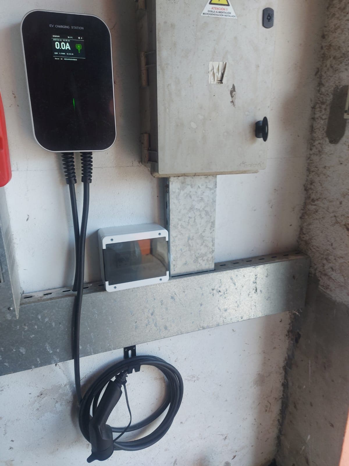 Wallbox installed next to a home electrical panel, with the cable hanging on its holder